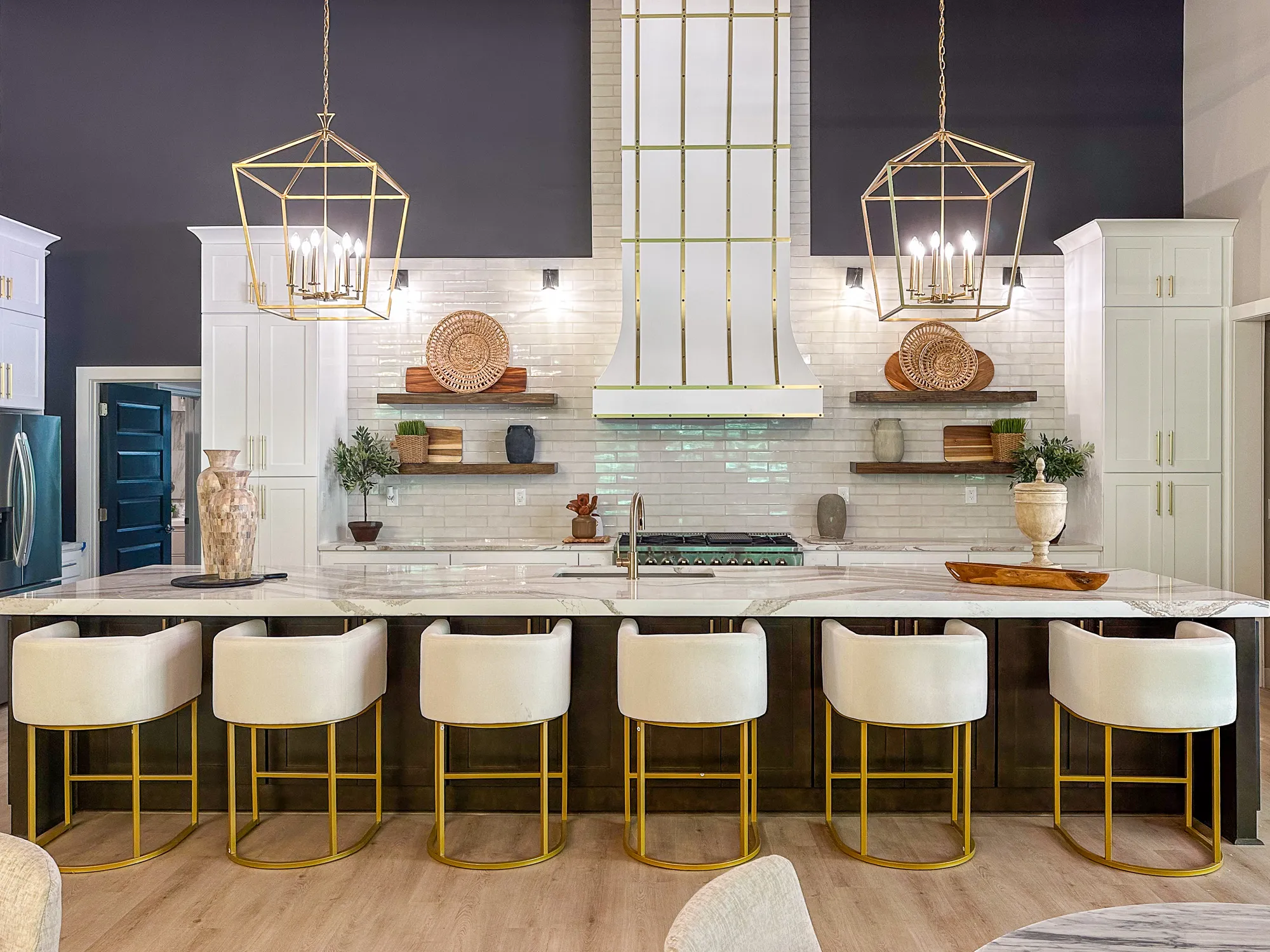 A kitchen island with six stools, brass lanterns, and a white range hood