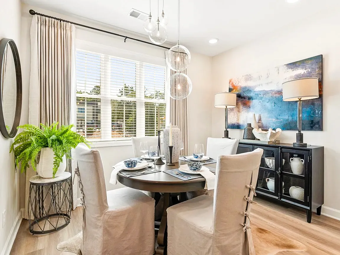 A dining room with a round table, linen chairs, and glass globe lights